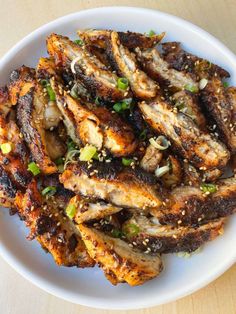 a white plate topped with chicken wings covered in sesame seeds and garnished with green onions