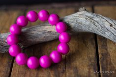 a pink beaded bracelet sitting on top of a piece of driftwood next to a branch