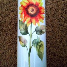 a white vase with a painted sunflower on the side sitting on carpeted floor