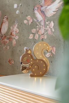 a wooden toy squirrel on top of a white table next to a wall with flowers