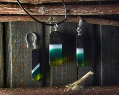 two pieces of glass are hanging on a wooden wall next to a pair of earrings