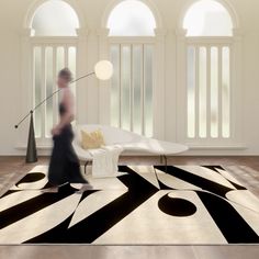 a woman walking across a living room with black and white rugs on the floor