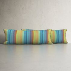 two striped pillows sitting on top of a white table next to a wall with a plant