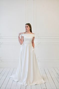 a woman in a white wedding dress posing for the camera with her hand on her shoulder