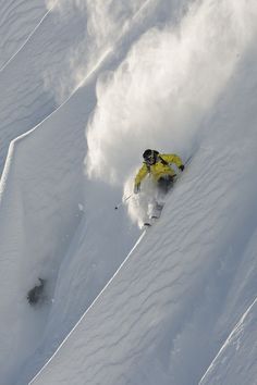 a person on skis going down a snow covered slope with powder coming from behind them