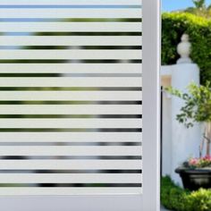 a window with vertical blinds on it in front of a white fence and potted plants