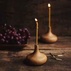 two candles sitting on top of a wooden table next to grapes and a bowl of grapes