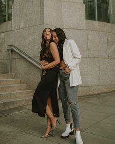 two women standing next to each other in front of a building