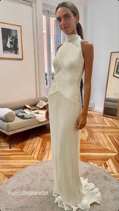 a woman standing in a room wearing a white dress with high neck and pleated skirt