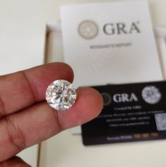 a hand holding a diamond in front of a box with a business card on it