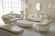 a living room filled with white furniture next to a large window and a mirror on the wall