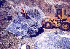 a man standing on top of a large rock next to a bulldozer in the mountains