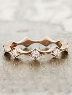 a rose gold wedding band with three diamonds on the top and bottom, sitting on a stone surface