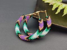 ✔️ Enhance your boho and hippie style with these exquisite handmade beaded hoop earrings. Made from high-quality glass materials, these earrings feature a stunning combination of green and purple beads that are meticulously handcrafted to create a unique and eye-catching design. With a size of 1.6 inches, they are the perfect accessory to add a touch of bohemian charm to your everyday outfits or special occasions. ✔️ Highlights: 1. Handmade Item: These hoop earrings are lovingly handmade, ensuri Beaded Hoop Earrings Native American, Hoop Beaded Earrings, Hippie Mode, Earrings Native American, Hippie Stil, Purple Beaded, Purple Beads, Earring Stand, Earrings Bohemian