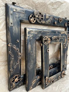 an old frame with gears and wheels on it sitting on a white wall next to another piece of art