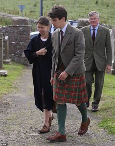 a man in a kilt walking down a path with two other men behind him