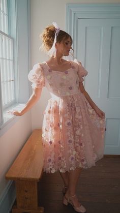 a woman in a pink dress standing next to a window