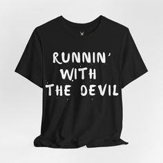 The "Runnin' with the Devil" unisex t shirt is a nod to rock 'n' roll rebellion. Perfect for music lovers and those who embrace their wild side, this tee captures the essence of classic rock with its edgy design. The bold text pops against the fabric, making a statement that's both daring and timeless. Whether you're hitting a concert, hanging out with friends, or simply want to showcase your rock-inspired style, this t shirt is the perfect choice for adding a rebellious edge to your wardrobe. SHABBY RABBIT T SHIRTS Discover unique, high-quality apparel at The Shabby Rabbit, your go-to destination for stylish and quirky t-shirts. We specialize in creating fun and original designs that cater to every personality, from vintage-inspired graphics to modern, edgy prints. Whether you're looking Black Punk T-shirt With Slogan, Grunge Slogan T-shirt For Streetwear, Slogan T-shirt For Alternative Fashion, Relaxed Fit T-shirt With Text Print For Music Festivals, Punk Style Pre-shrunk Short Sleeve Shirt, Grunge Short Sleeve T-shirt For Concert, Unisex Punk T-shirt With Letter Print, Rock Style T-shirt With Letter Print And Short Sleeves, Relaxed Fit Graphic T-shirt For Concerts