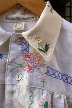 a white shirt with colorful flowers on it and a wooden hanger in the background