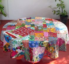 a round table covered with multicolored cloths and potted plants in the background