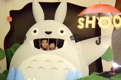 two people are looking out from behind a fake bunny with an umbrella in front of them