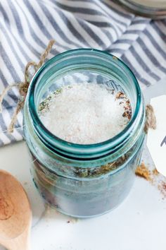 a glass jar filled with white stuff sitting on top of a table next to a wooden spoon