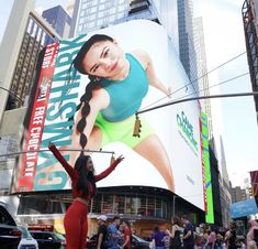 a woman standing in front of a giant billboard on the side of a building with her arms up