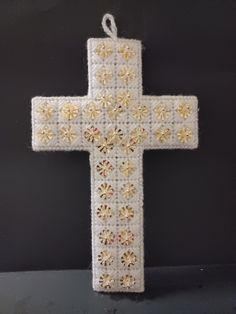 a white cross hanging from the side of a black wall with gold flowers on it