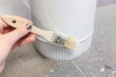 a person is holding a paint brush near a white container that has been placed on the ground