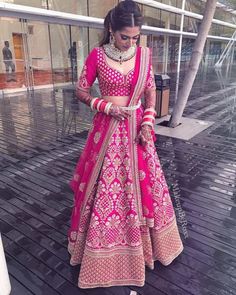 a woman in a pink lehenga standing on a wooden floor next to a building