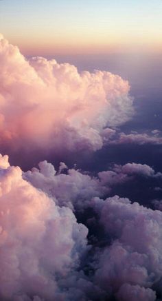 the view from an airplane looking down on some clouds and blue sky with pink hues