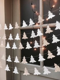 paper christmas trees are hanging from a string in front of a window with fairy lights