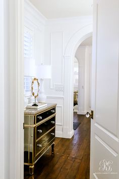 an entry way with white walls and wood flooring in the hallway, along with a black chest of drawers