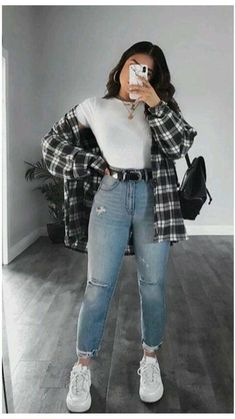 a woman taking a selfie while wearing ripped jeans and a plaid jacket with white sneakers