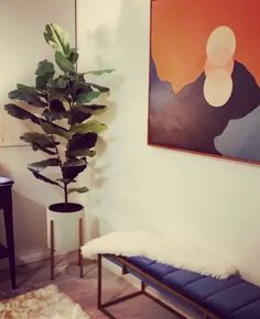 a living room with a couch and a painting on the wall above it, next to a plant