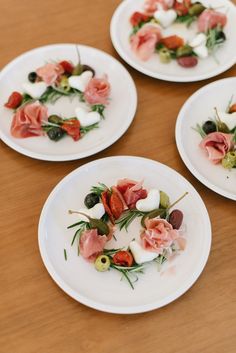 four white plates topped with appetizers on top of a wooden table