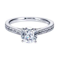 a white gold engagement ring with an engraved band and a round cut diamond in the center