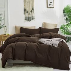 a bed with brown sheets and pillows in a white room next to a potted plant