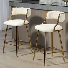 two white and gold bar stools sitting in front of a counter top with a vase on it