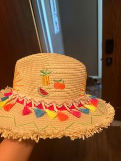 a person wearing a straw hat with tassels and fruit embroidered on the brim