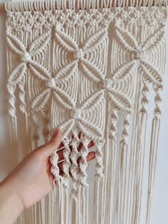 a hand is holding the end of a macrame wall hanging with white yarn