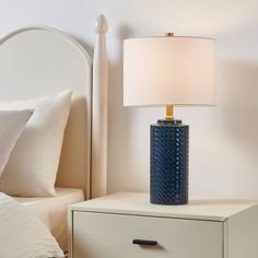 a blue lamp sitting on top of a night stand next to a white dresser and bed