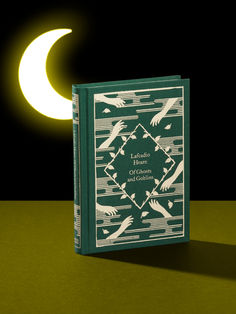 a green book sitting on top of a table next to a half moon and a black background