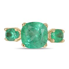 A Colombian emerald three stone ring. This bespoke ring design is crafted in gleaming 14K yellow gold, this ring features a 6.55-carat cushion cut in its center. Oval emeralds are flanked on the side creating an array of green. Simply gorgeous and one of a kind! Setting: Three-Stone Metal Purity: 14K Yellow Gold Center Stone: Emerald Shape: Cushion Cut Estimated Center Weight: 6.55-Carats Clarity: Semi-Transparent Color: Green Luster: Very Good Origin: Colombia Treatments: Natural Side Stones: E Heirloom Style Three Stone Green Emerald Ring, Heirloom Green Emerald Ring With Three Stones, Heirloom Three-stone Emerald Ring, Green Emerald Three Stone Ring In 14k Gold, Three Stone Emerald Ring In 14k Gold, Luxury Gold Emerald Ring With Three Stones, Green Three-stone Birthstone Ring In 14k Gold, Green Three Stone Birthstone Ring In 14k Gold, Formal Gold Emerald Ring With Three Stones