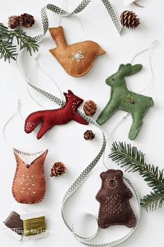 christmas ornaments made from felt and pine cones on a white surface with evergreen branches, pine cones, and other decorations