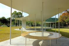 a circular wooden table sitting in the middle of a park next to tall white poles