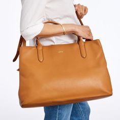 Super-functional and decidedly beautiful, the Caroline Leather Handbag is the ultimate work carryall. Spacious enough to fit a 13" laptop and everything else you need from 9 to 5, this versatile bag goes with everything, making it the perfect addition to your work wardrobe. Swap out the matching leather crossbody strap for one of our many colorful straps to create your own style.    17"w x 6"d x 11.25"h  Leather with a soft linen lining and gold-toned hardware.  See Product Information for more Everyday Leather Bag, Straw Beach Bag, Large Crossbody Bags, Bow Bag, Mark And Graham, Work Tote, Boho Bags, Personalized Tote Bags, Black Leather Tote