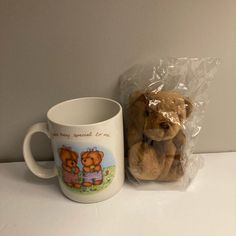 a teddy bear sitting next to a coffee mug on a counter with plastic wrap around it