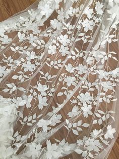 the sheer fabric has white flowers and leaves on it, along with wooden flooring