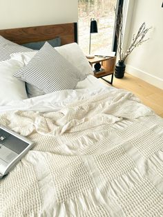 an open laptop computer sitting on top of a white bed covered in blankets and pillows